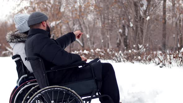 Disabled couple, man and woman, are sitting at wheelchairs together spending time at park in winter