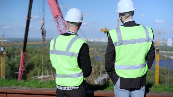 Back View Portrait of Two Positive Young Men in Uniform Talking Looking at Industrial Park and