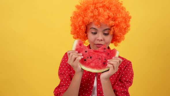 Amazed Hungry Child in Fancy Orange Hair Wig Eat Water Melon Slice on Yellow Background Hunger