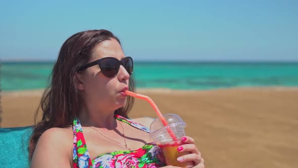 Young Woman Drinking a Fruit Cocktail on the Shore of the Azure Sea