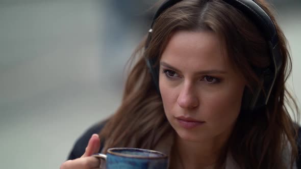 Coffee Lover Woman Is Sipping Hot Drink and Listening To Song By Headphones, Closeup Portrait in