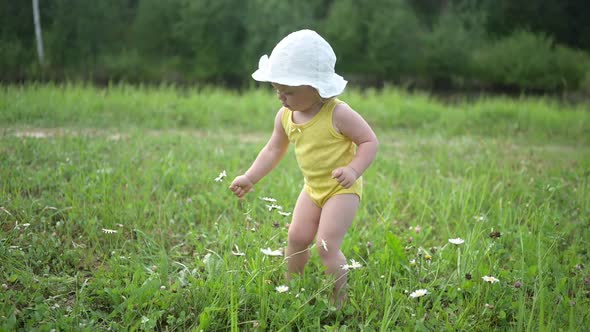 Little Funny Cute Blonde Girl Child Toddler in Yellow Bodysuit and White Hat Walking in Field with