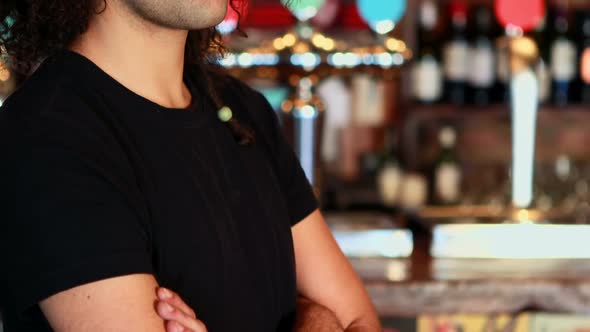 Portrait of barman standing with arms crossed at bar counter