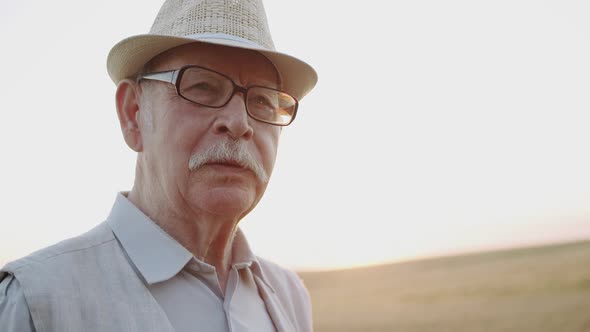 Portrait of Senior Man Eats Fresh Bread and Has Pleasure in Sunny Wheat Field