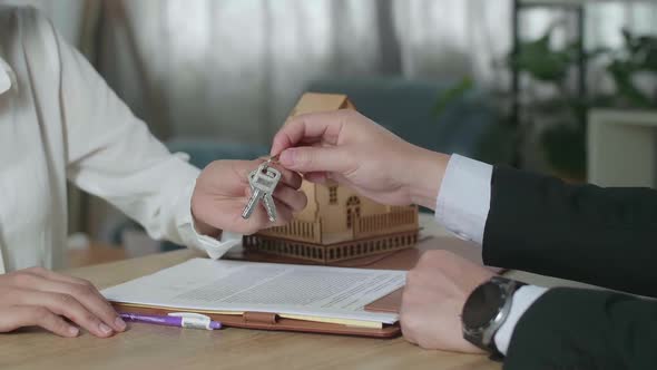 Close Up Of Real Estate Agent With House Purchase Contract Paper Giving The Keys To A Woman