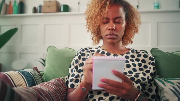 Young Ethnic African American Woman Writes Shopping List in Notebook and Smiles