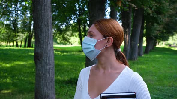 Young Woman Walks Alone in the Park in a Mask. 