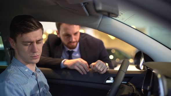 Handsome Young Man Behind the Wheel of New Car in Auto Dealership.