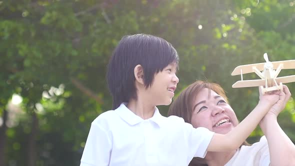 Cute Asian Mother And Son Playing Wooden Airplane Together In The Park Outdoors