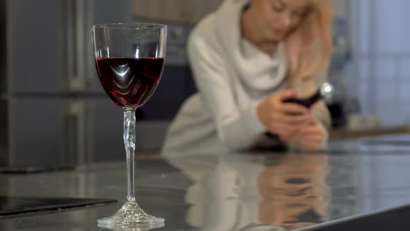 Red Wine in a Glass on the Table, Woman Holding a Bottle on the Background