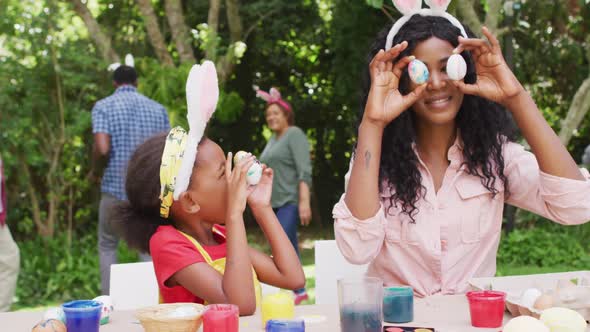 Animation of happy african american mother and daughter painting easter eggs outdoors, having fun