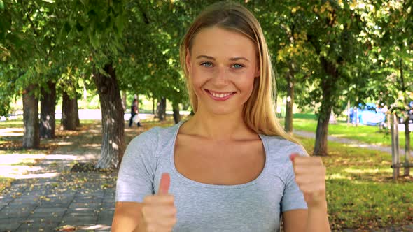 Young Pretty Blond Woman Shows Thumbs Up on Agreement - Park with Trees in Background