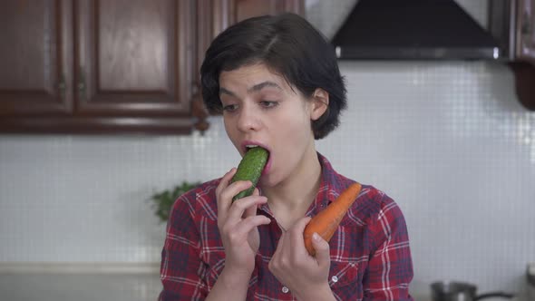 Portrait of Pretty Young Girl Biting and Chewing First a Big Cucumber, and Then a Fresh Carrot