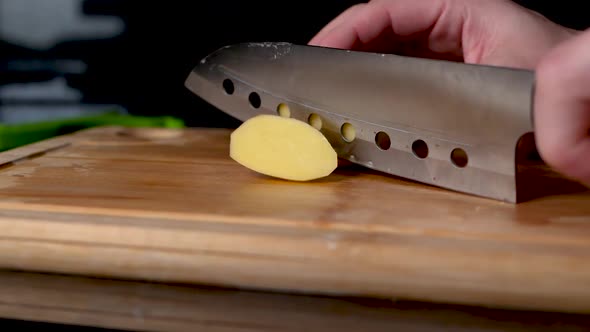 Close up shot of a silver knife chopping a potatoe, camera slides.