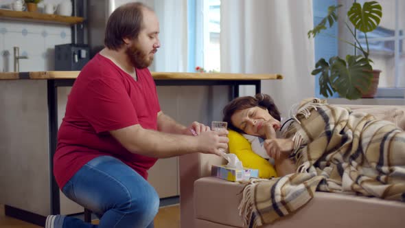 Adult Man Bringing Glass of Water for Sick Aged Mother Lying on Couch