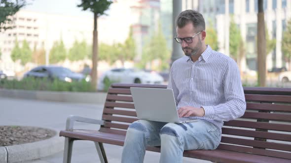 Rejecting Young Adult Man in Denial While Using Laptop Sitting Outdoor on Bench