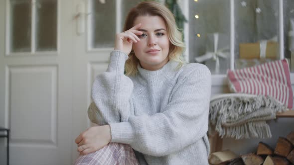 European Young Attractive Woman in Warm Sweater Sits in the Scandinavian Interior and Looks To the