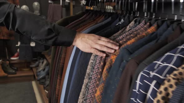 A Man Runs His Hand Over Multi-colored Jackets on a Hanger in a Store. Choosing a Suit in a Tailor