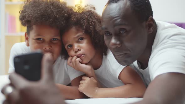 Happy African American Father with Little Son and Daughter Taking Selfie on Smartphone at Home