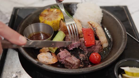 Cutting Roasted Beef Steak Served With White Rice, Grilled Prawns, And Vegetables. close up