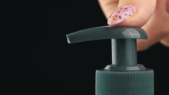 Woman Pushes Dispenser and Liquid Soap Flows Into Her Hand on Black Background