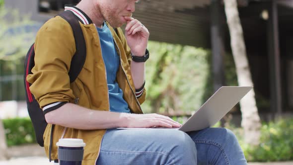 Thoughtful albino african american man with dreadlocks sitting in park using laptop