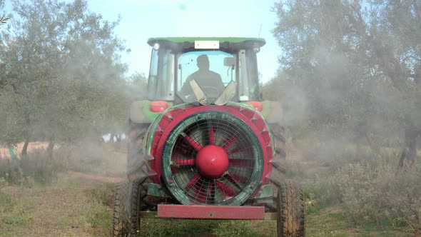 Rear view of a tractor spraying or fertilizing an olive grove with chemicals