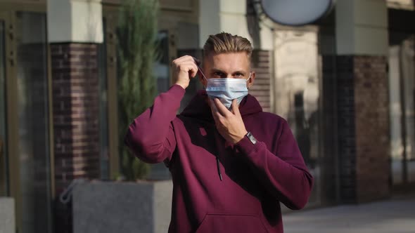 Portrait of Young Man Looking at the Camera and Putting Medical Mask on Face for Protection Against