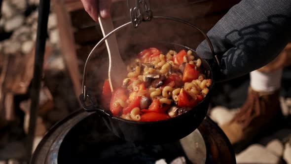 Pasta with Mushroomsand Onions are Fried in a Pan Over a Fire in the Field