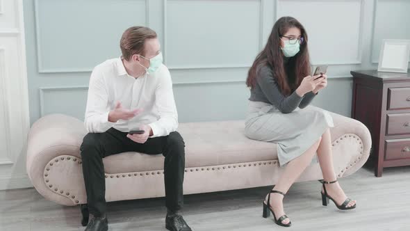 Young american business man and woman in face mask using smart phone with colleague on sofa.