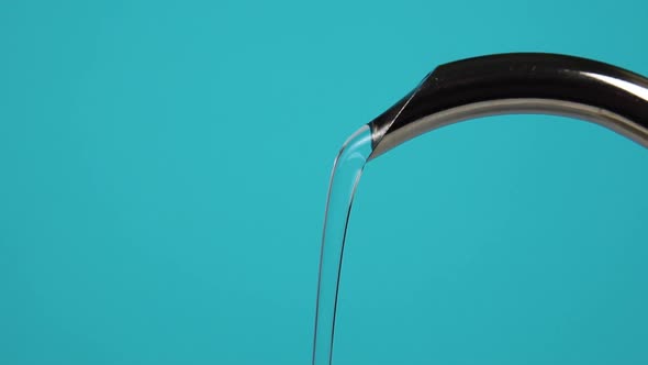 A stream of clean water from a metal jug with a narrow spout pours in slow motion