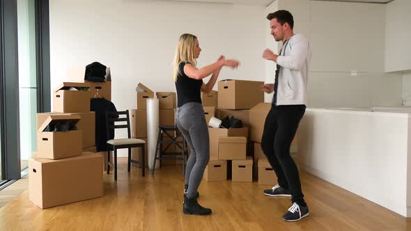 A Happy Moving Couple Dances in a New Apartment, Finishes with Smiles and Fingerpointing at Camera