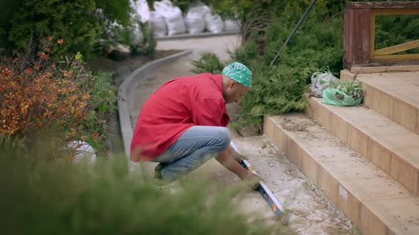 Side View of Concentrated African American Man Measuring Backyard Porch with Level Ruler Outdoors