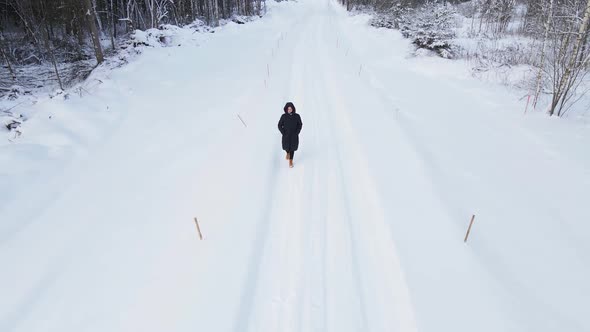 Dolly Out Woman in Black Walking Along Village Road Covered in Snow in Winter