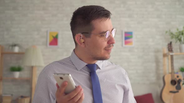 Man with a Hearing Aid in His Ear in the Living Room Talking on a Smartphone