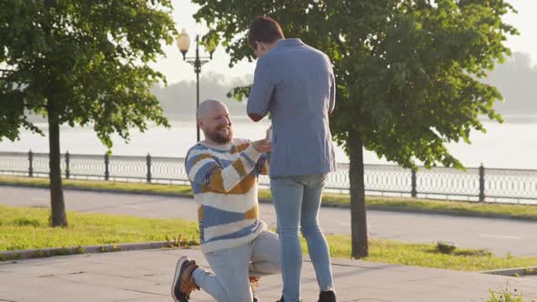 Guy Gifts a Wedding Ring To His Fiance Standing on His Knee. Gay Marriage Proposal Concept