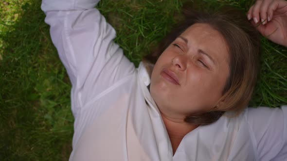 Top View Portrait of Unsatisfied Caucasian Sad Plussize Woman Lying on Green Grass Thinking