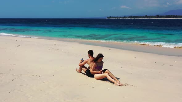 Man and woman sunbathing on tranquil island beach voyage by shallow ocean and clean sandy background