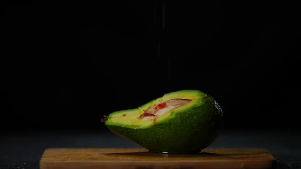 White Salt Falling in Slow Motion on Green Avocado Covered with Olive Oil