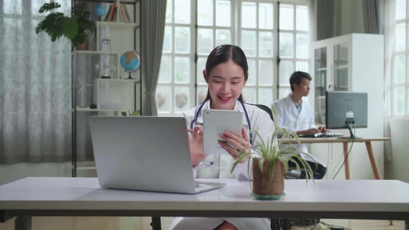 Young Asian Woman Doctor Is Using Tablet While Work With Laptop Computer In Workplace