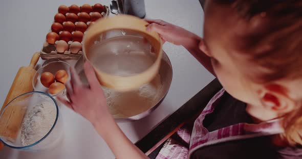 Woman Sifts Flour Through Sieve in the Kitchen While Baking Croissants