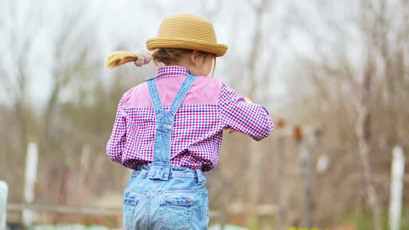 a Funny Little Girl in a Hat Eats Green Onions and Waves at the Sharpness