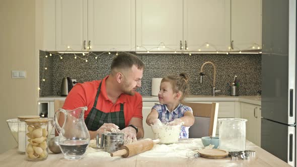 Dad and Daughter 5-6 Years Old Knead Dough in the Kitchen. The Father Treats His Child with Great