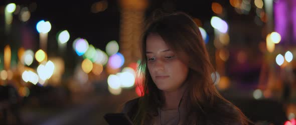 A young woman listening to the music on her phone in the middle of a street