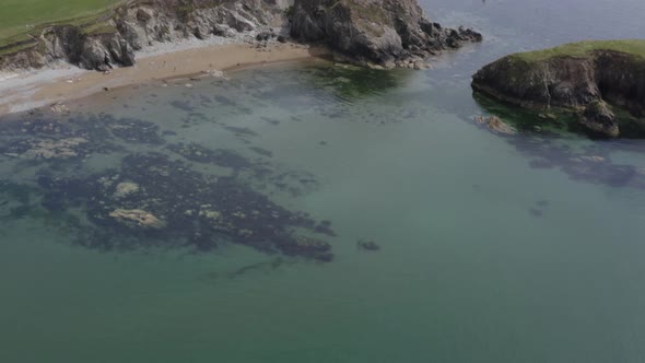 Aerial tilt reveals green pasture land atop ocean cliffs, blue horizon