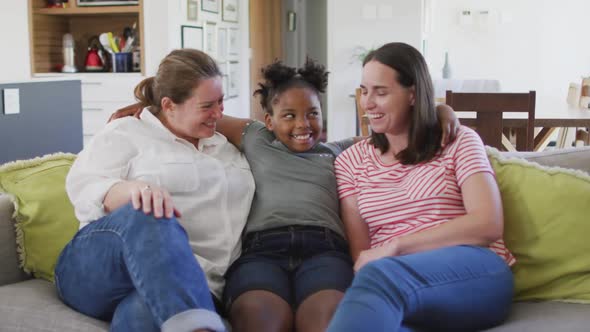 Portrait of happy caucasian lesbian couple and their african american daughter embracing and smiling