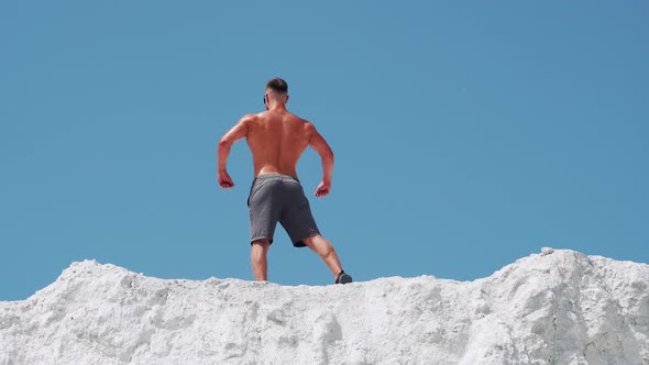 Bodybuilder athlete posing with muscles in nature against a blue sky