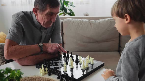 Elderly Senior Grandfather Learning a 4 Year Old Child Playing Chess Sitting at a Table