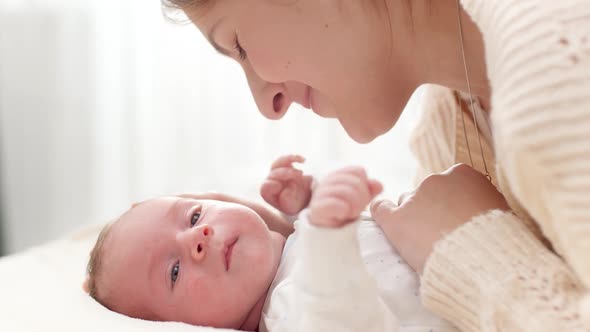 Cute Newborn Baby Boy Lying with Young Mother on Bed Against Big Window on Sunny Morning