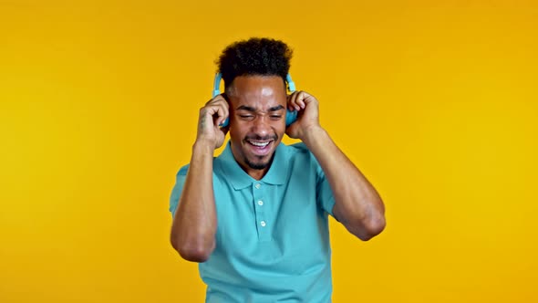 Handsome African Man Having Fun, Dancing with Blue Headphones in Yellow Studio. Music, Dance, Radio